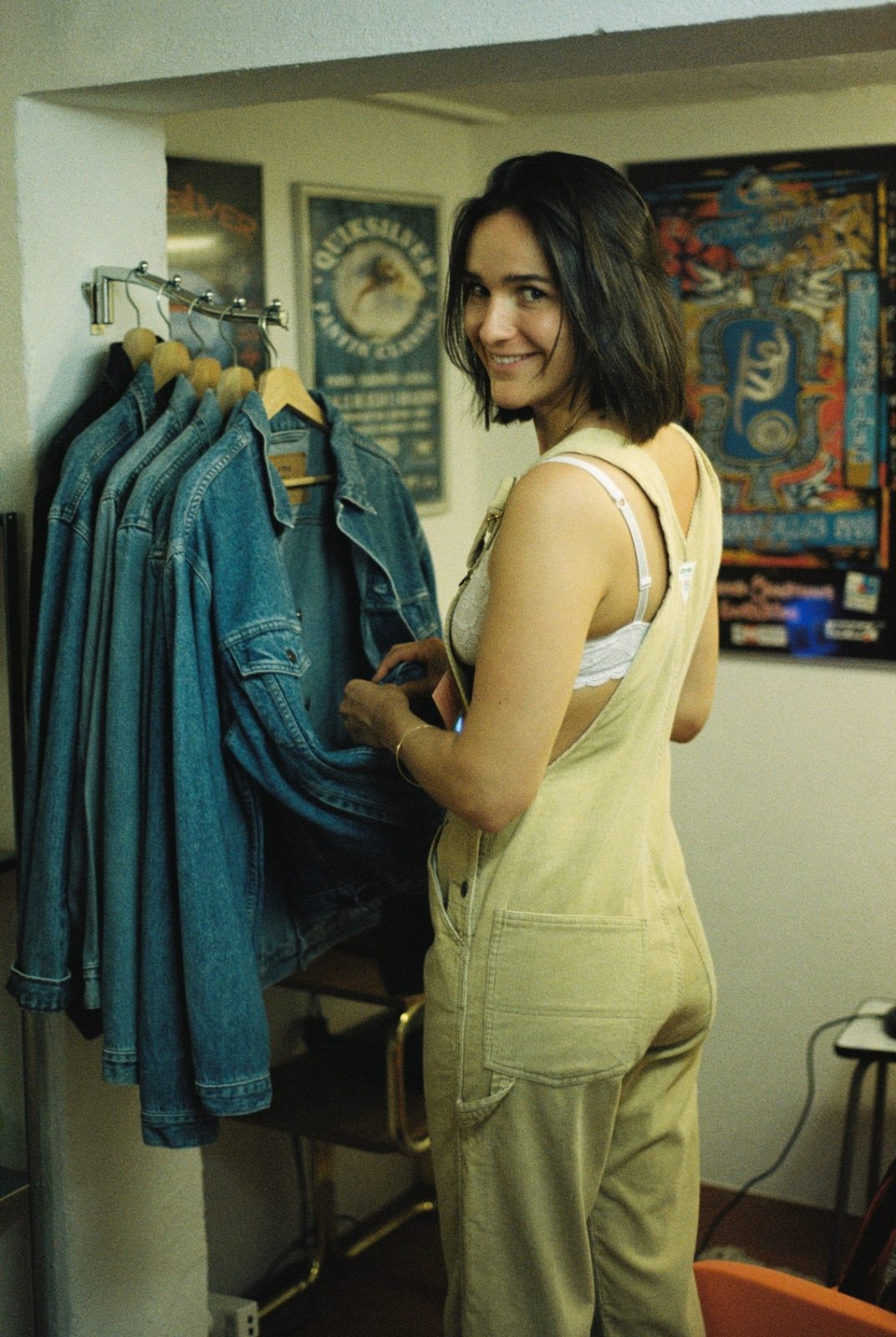 A smiling woman looking back over her shoulder while browsing a rail of denim jackets.